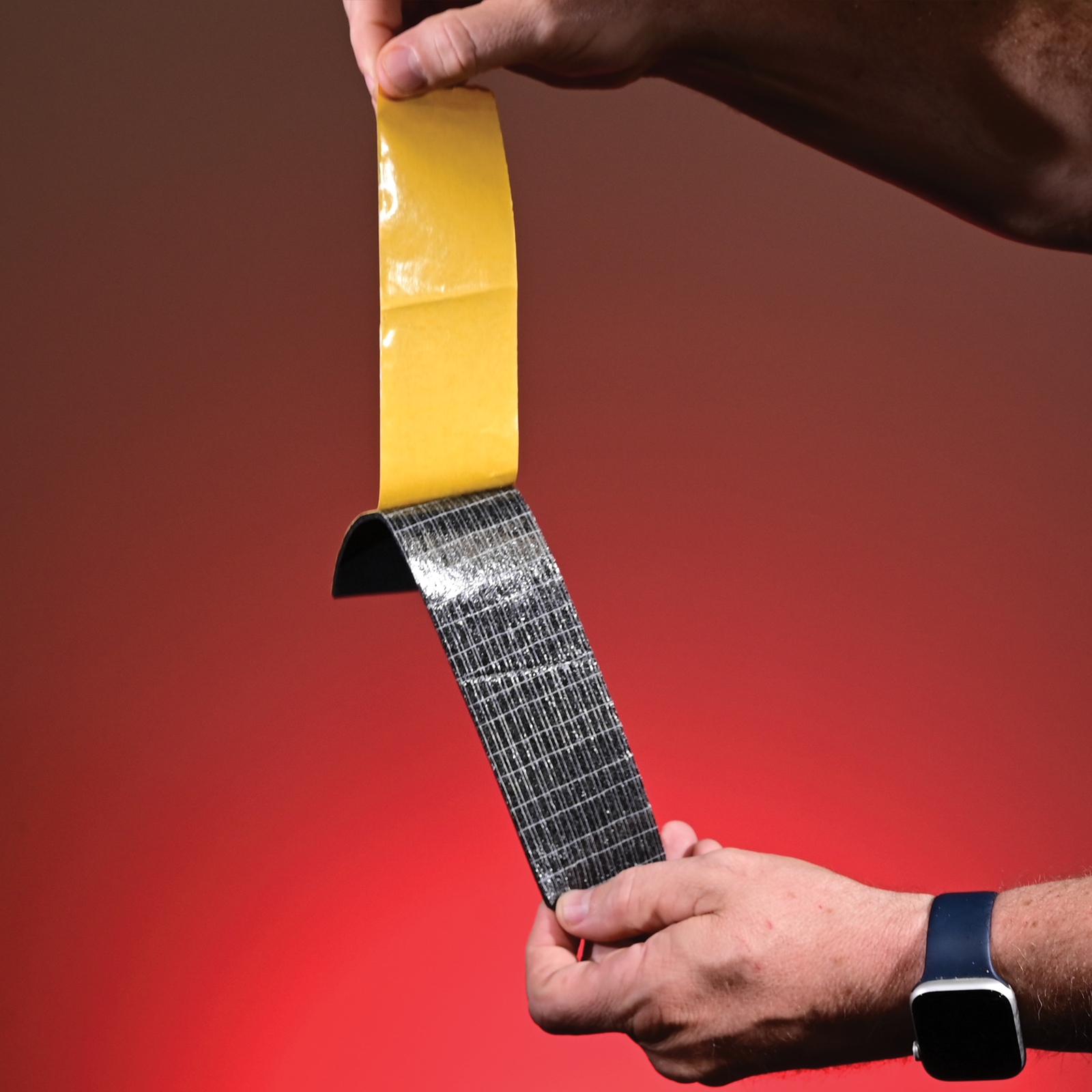 Hands peeling the yellow release liner away from the scrim foam tape to reveal the adhesive.
