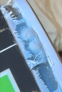 A close-up photo of the bottom seam of an aerosol can with a thin film of Bird Dog Leak Detector applied, showing tiny, sustained bubbles forming along the seam.