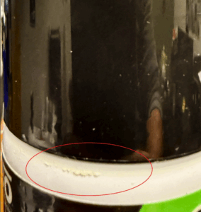 A close-up photo of an aerosol can showing a faint, dried ring of product residue underneath the cap.